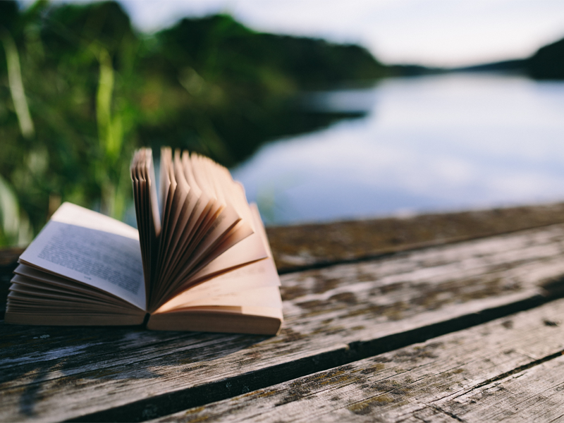 Open book on a wooden dock by a lake