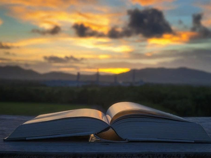 An open book on a wooden surface against a sunset sky